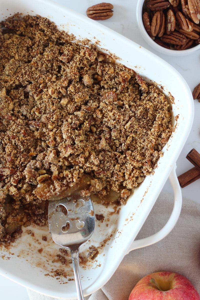 healthy apple crisp in white baking dish with silver pie server