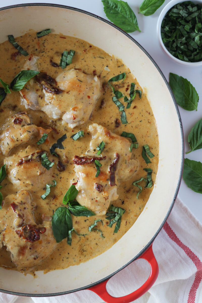 Dairy-free marry me chicken thighs in ceramic coated cast skillet topped with fresh basil