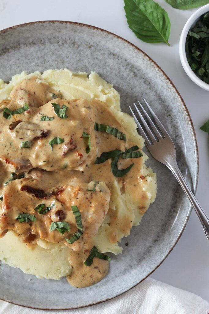 Healthy marry me chicken on bed of mashed potatoes on plate garnished with fresh basil