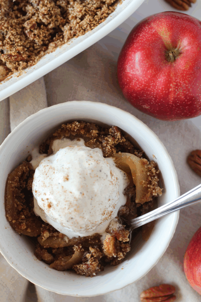 serving of healthy apple crisp with a scoop of vanilla ice in small white bowl with spoon