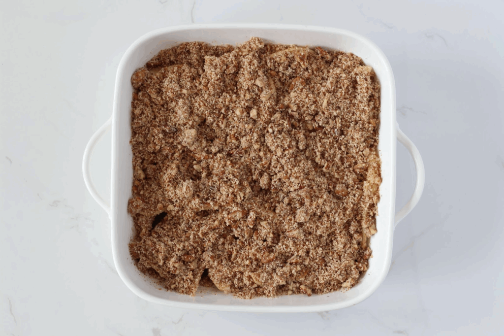 pecan topping spread out evenly over sliced apples in white baking dish