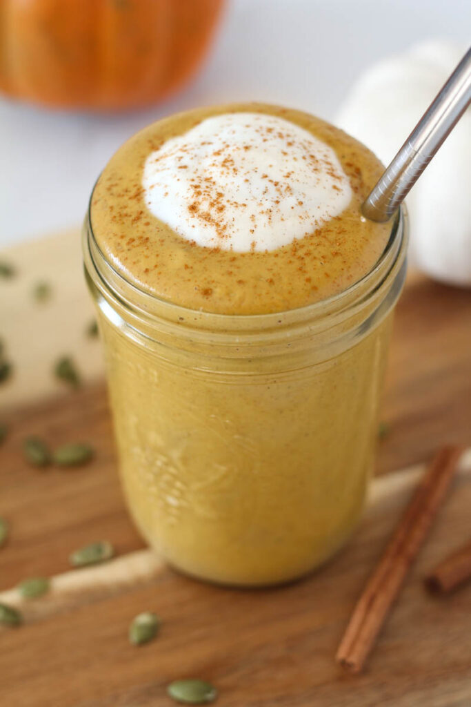 protein pumpkin smoothie in mason jar garnished with spoonful of coconut cream and sprinkle of cinnamon with stainless steel straw