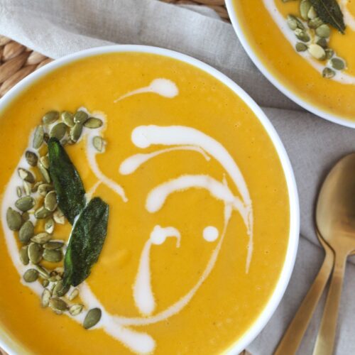 roasted butternut squash and apple soup in white bowl topped with coconut milk swirl, pepitas, and sage leaves