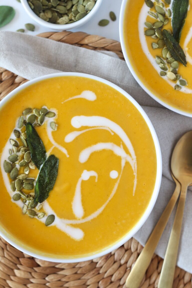 roasted butternut squash and apple soup in white bowl topped with coconut milk swirl, pepitas, and sage leaves