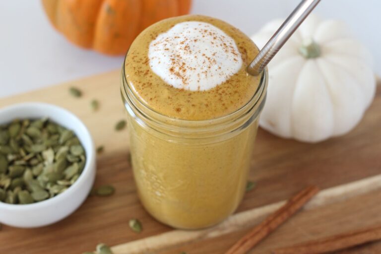 pumpkin protein smoothie in mason jar toped with cinnamon and coconut cream with stainless steel straw sitting on wooden board