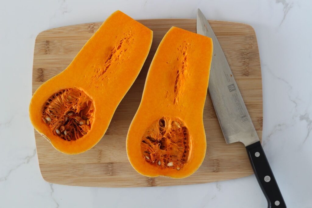 Sliced butternut squash halves on wooden cutting board with knife