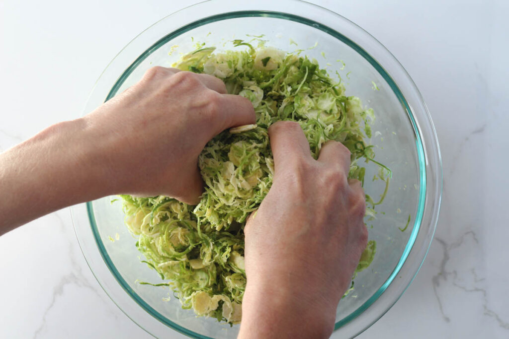 massaging shredded Brussels sprouts with hands in glass bowl