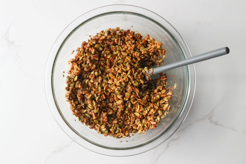 mixing granola ingredients in glass bowl with small gray spatula