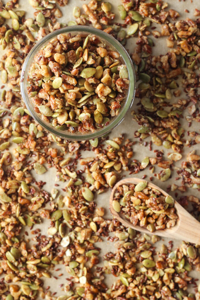 small jar of pumpkin seed granola on baking sheet with granola and a wooden spoon 