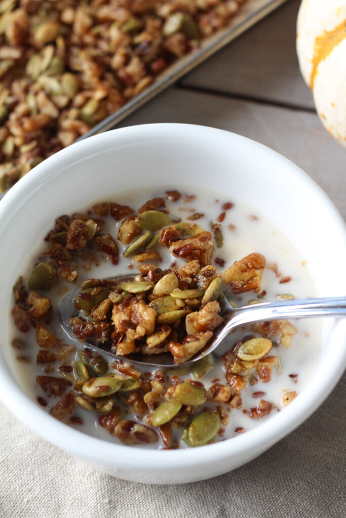 serving of pumpkin seed granola in small white bowl with a metal spoon