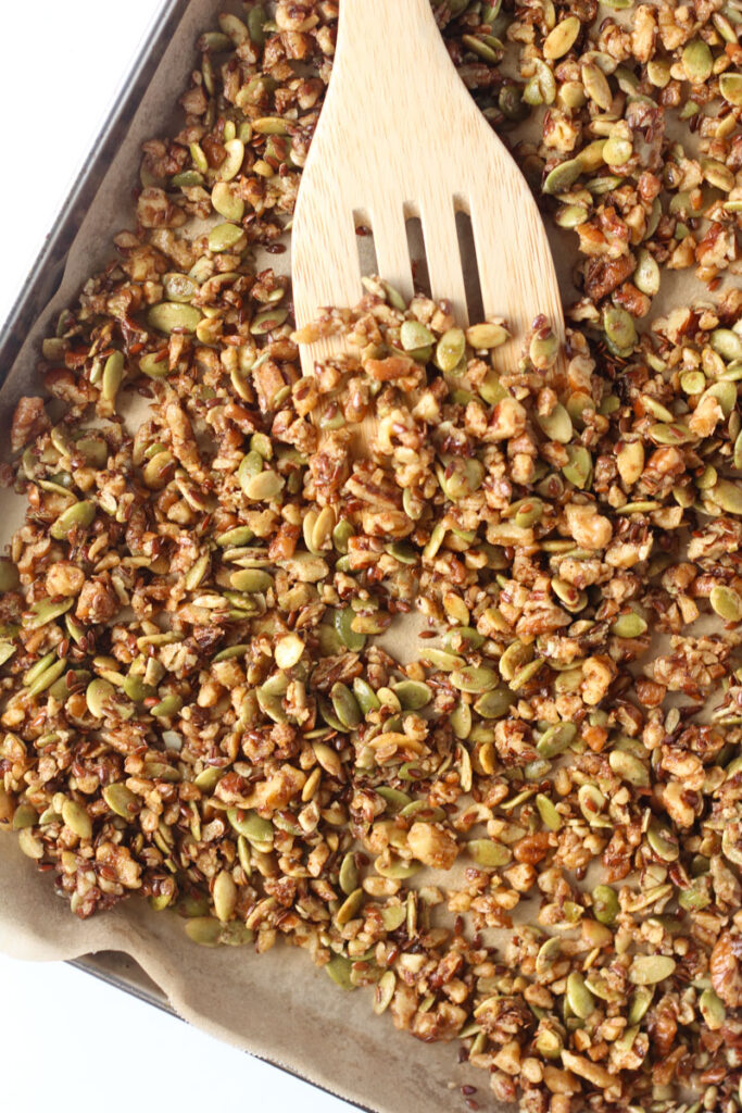 Pumpkin seed granola on baking sheet lined with parchment paper with wooden spatula