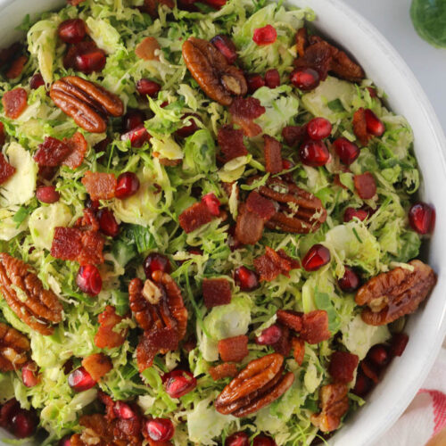 shaved Brussels sprouts salad with bacon, pomegranate, and pecans in white bowl
