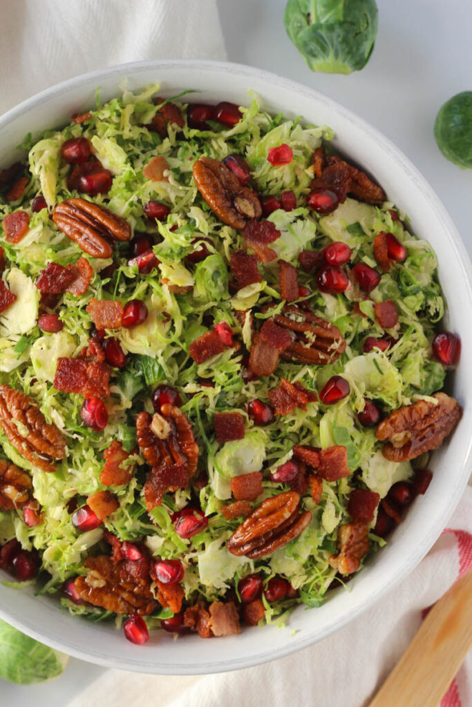 brussels sprouts salad with bacon, pomegranate, and pecans in white bowl