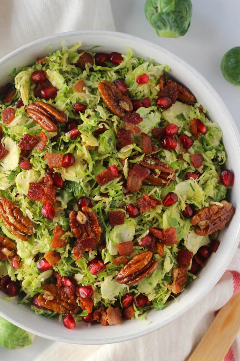 shaved Brussels sprouts salad with bacon, pomegranate, and pecans in white bowl