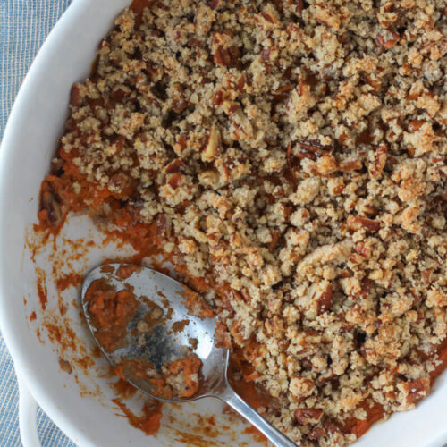 sweet potato casserole with pecan topping in oval white casserole dish with silver serving spoon