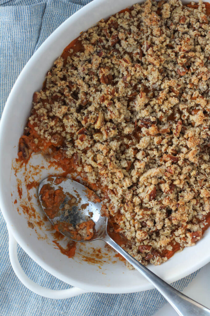 sweet potato casserole with pecan topping in oval white casserole dish with silver serving spoon sitting inside