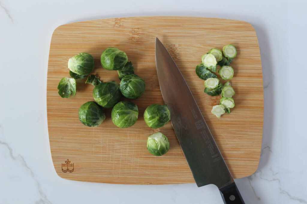 Trimming off Brussels sprouts stems with chef's knife on wooden board