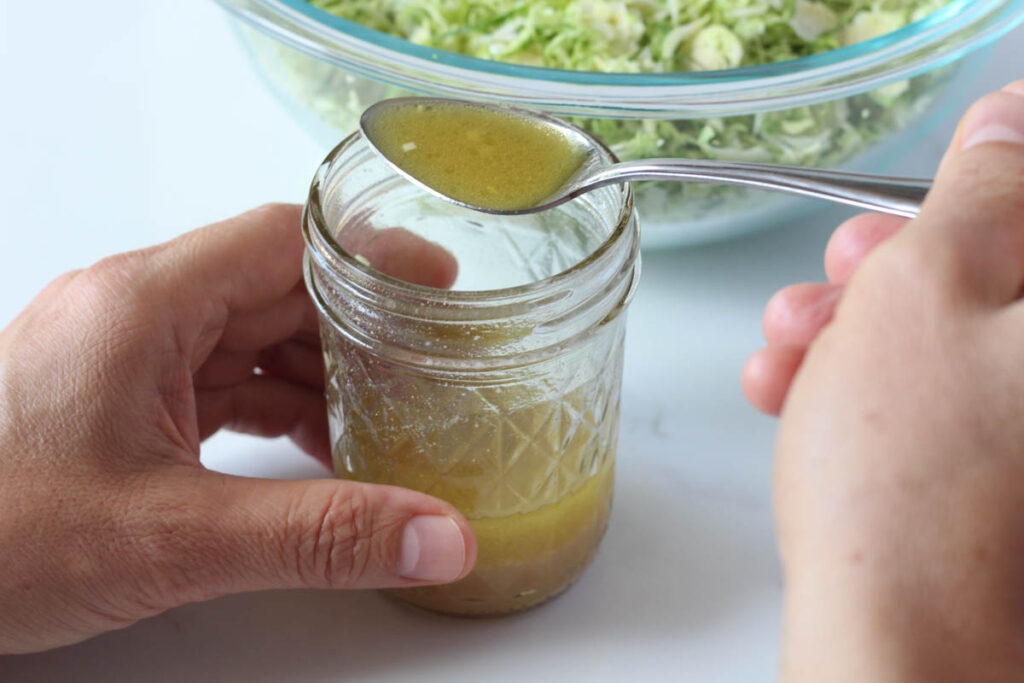 holding spoonful of apple cider vinaigrette over small mason jar