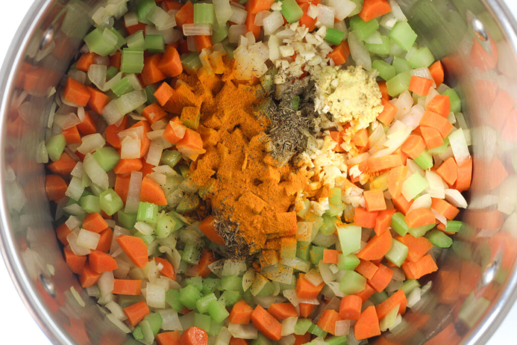 adding turmeric, ginger, garlic, and thyme to stockpot with veggies