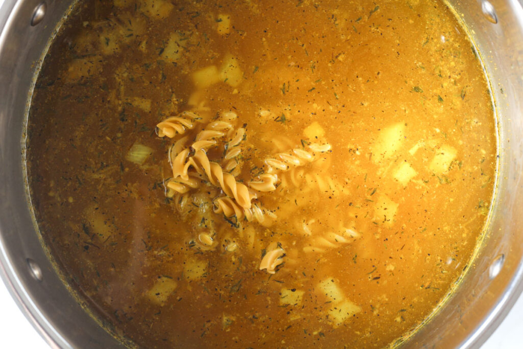 adding broth, chicken, noodles, salt, and pepper to stockpot