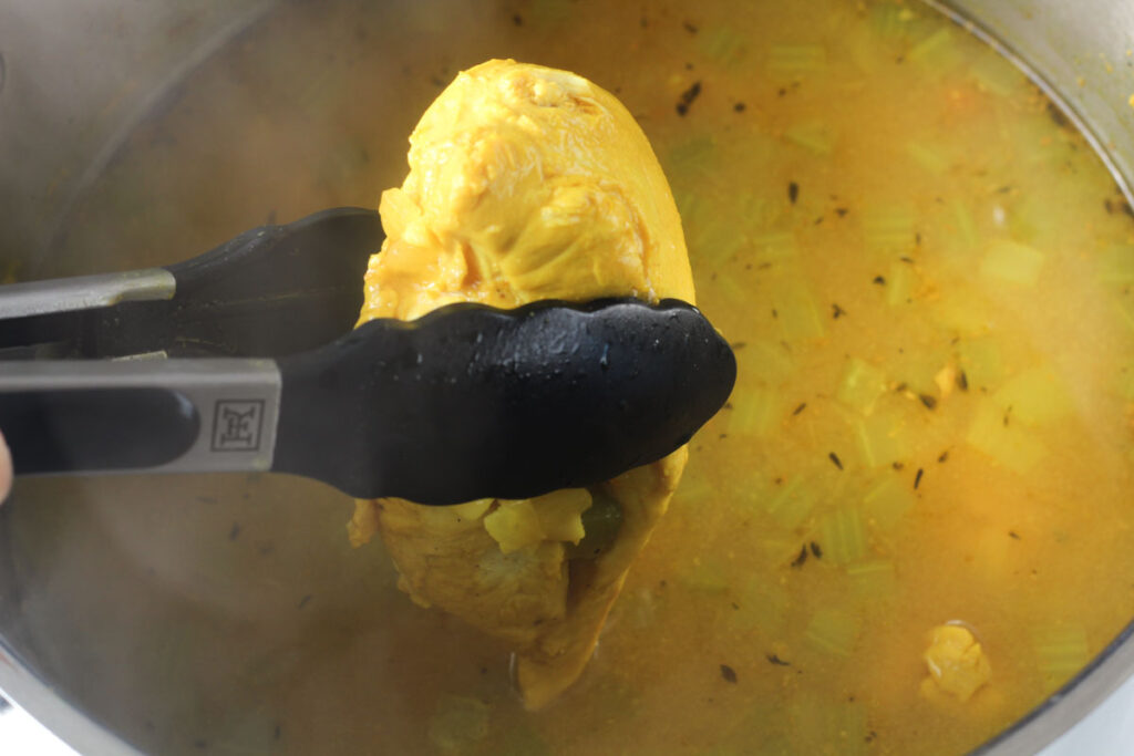 removing chicken breast from soup with tongs