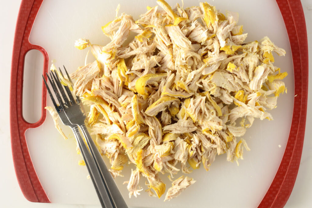 shredded chicken breasts on silicone cutting board with two forks