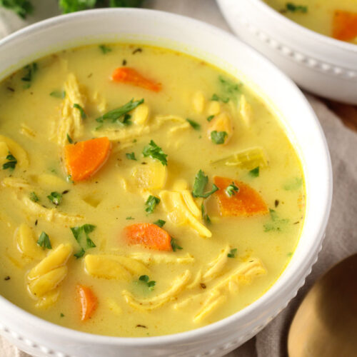 turmeric chicken noodle soup in small white bowl with spoon