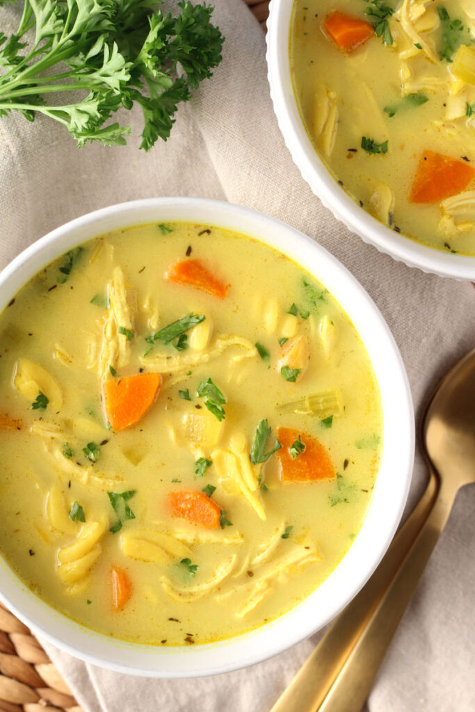 chicken noodle soup with turmeric and ginger in white bowl with garnished with fresh chopped parsley