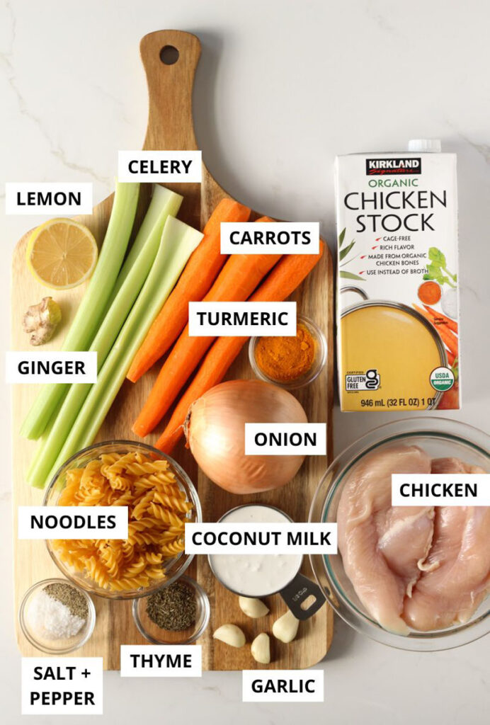turmeric chicken noodle soup ingredients on wooden board on marble counter labeled